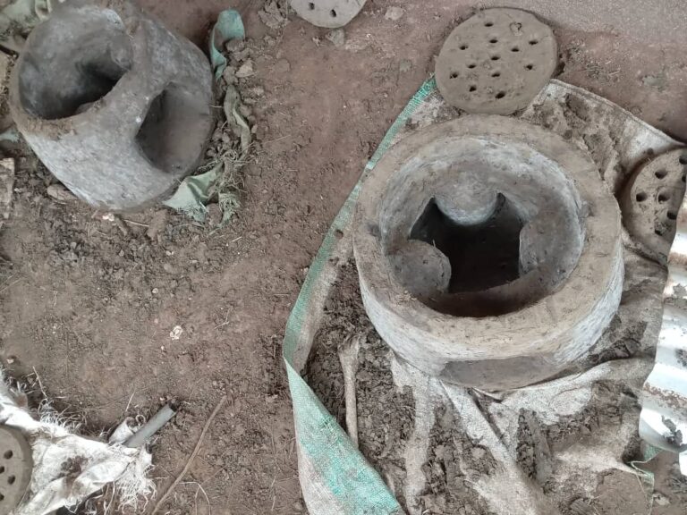 Deux foyers améliorés en argile sèchent au sol à côté de leurs grilles perforées
