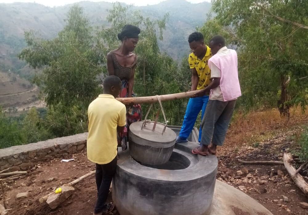 Quatre jeunes manœuvrent le couvercle d'un biodigesteur achevé, sur une colline dominant une vallée boisée
