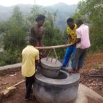 Quatre jeunes manœuvrent le couvercle d'un biodigesteur achevé, sur une colline dominant une vallée boisée